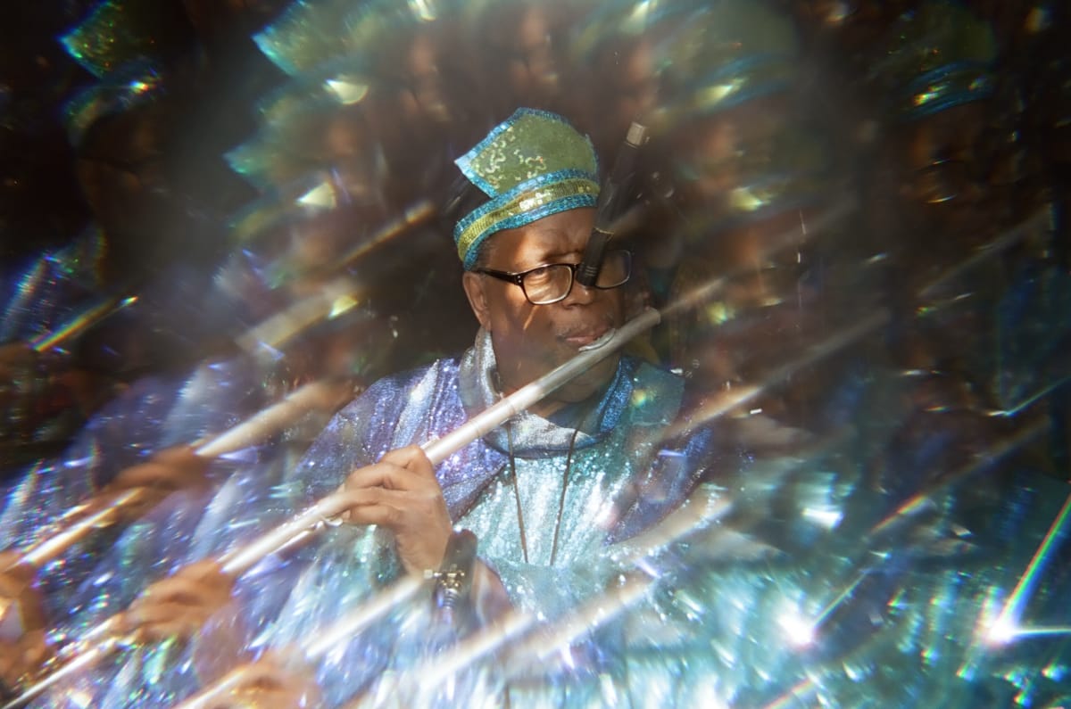 A Sun Ra Arkestra flutist in a sequined green-and-blue cap and shimmering blue robe plays at Union Pool, his image repeated in a ring of prismatic reflections.