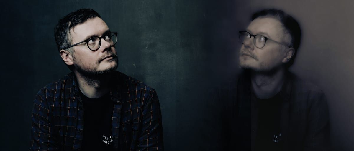 A diptych portrait of a man (Gavin Miller of worriedaboutsatan) in round glasses and a plaid shirt against a dark background, one image sharp and one motion-blurred. Photo by Jez Sheard.