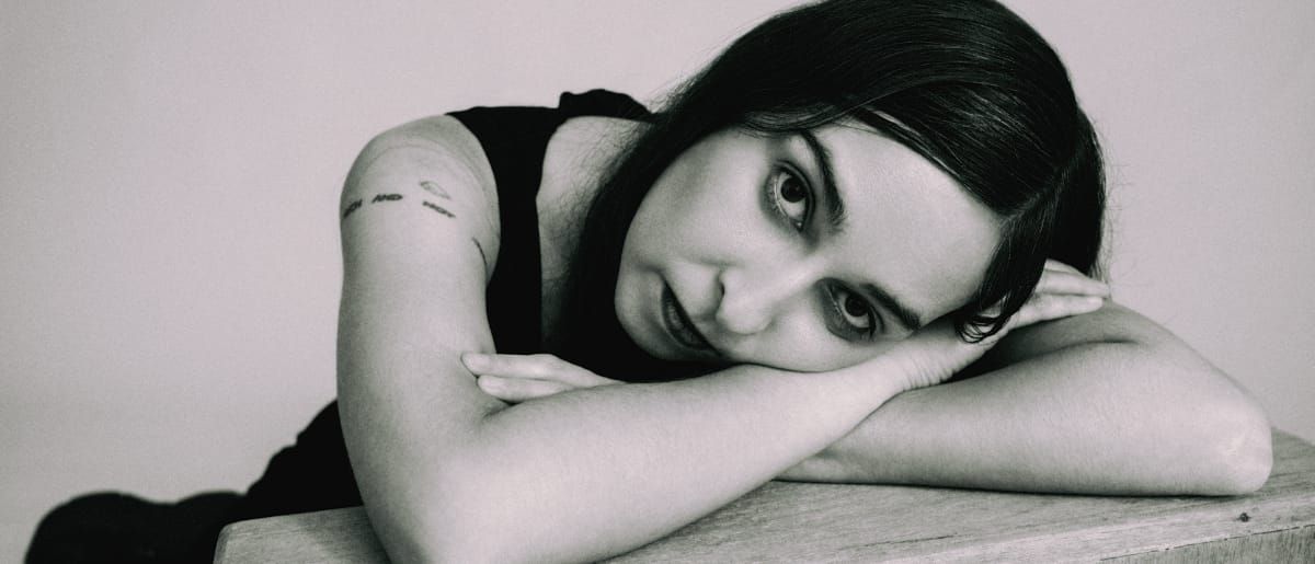 Concepción Huerta rests her head sideways on her folded arms on a wooden surface, looking directly at the camera, in black and white.