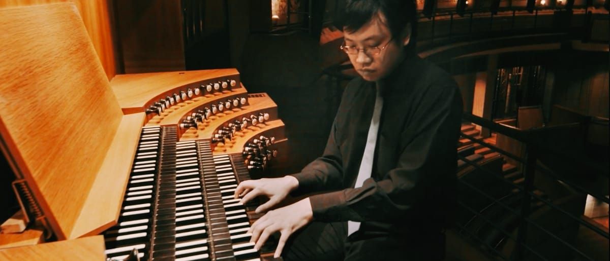 Phoon Yu plays a four-manual pipe organ, eyes on the keys, hands spread across two keyboards, rows of stop knobs angled beside him.