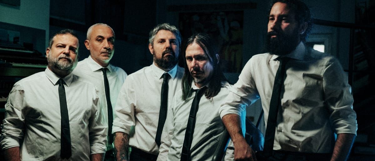 The five members of Calibro 35, in white shirts and black ties, stand shoulder to shoulder in a darkened studio, keyboards at the edge of the frame.