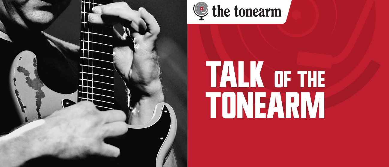 Black-and-white close-up of hands on a worn electric guitar's fretboard beside a red panel reading "Talk Of The Tonearm" under The Tonearm logo.