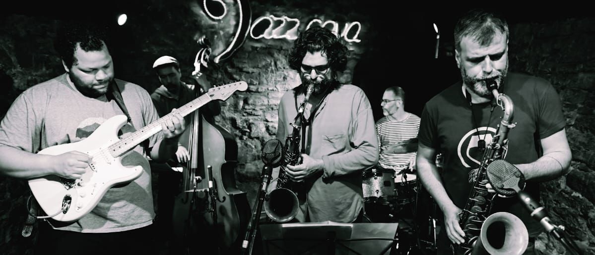Juanma Trujillo on guitar with band in black and white jazz club performance, saxophone and other musicians visible. Photo by Joan Cortès.