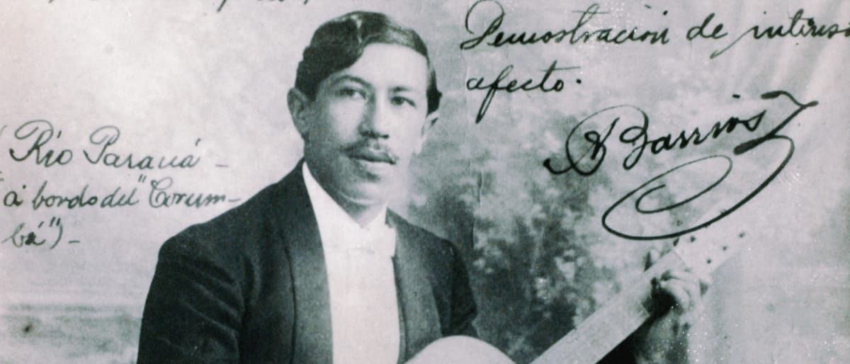 A vintage signed promotional photo of Agustín Barrios-Mangoré holding a guitar, with handwritten Spanish inscriptions and his signature overlaid on the image, circa 1910.