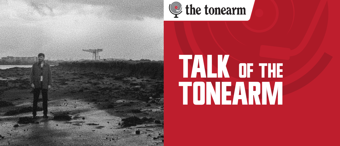 The Talk Of The Tonearm masthead: a red title panel beside a grainy black-and-white photo of a lone figure standing on a rocky tidal flat, a shipyard crane on the horizon.