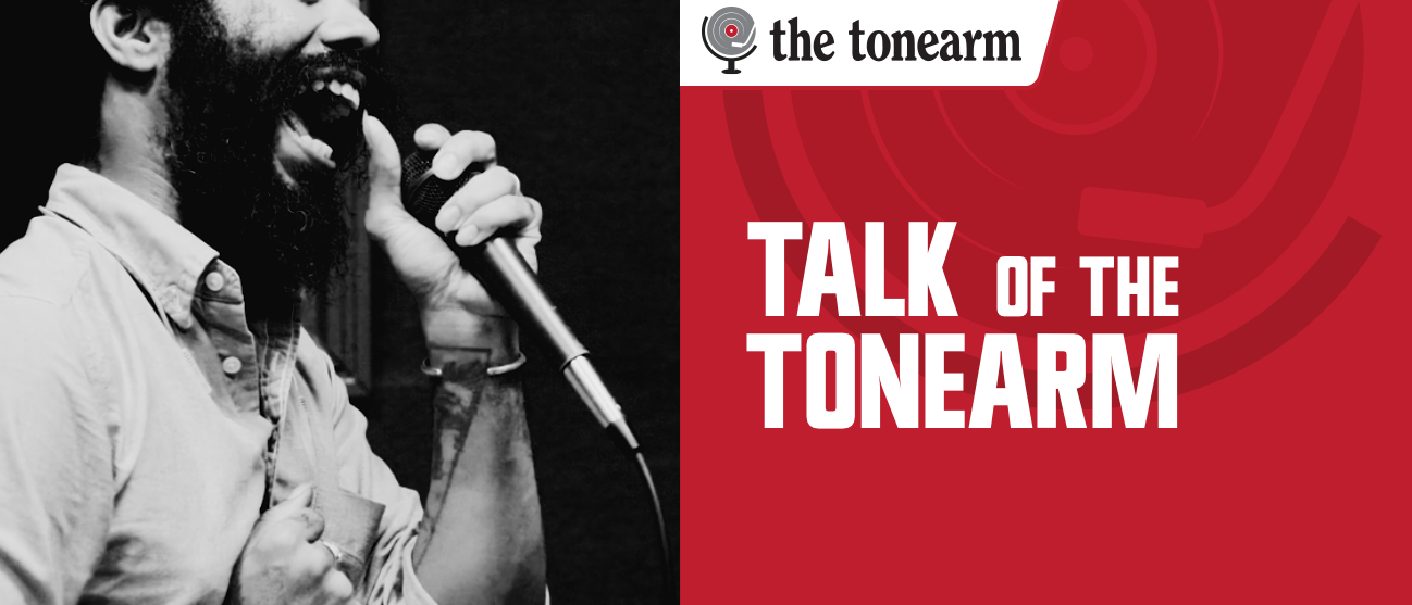 Robert Aiki Aubrey Lowe sings into a handheld microphone in black and white, beside a red panel carrying The Tonearm's logo and the words "Talk Of The Tonearm."