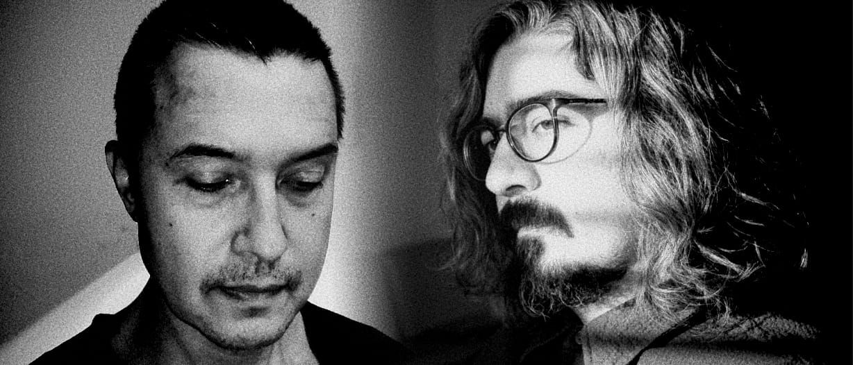 Black-and-white double portrait: Eugene Thacker, head lowered and eyes cast down, beside Siavash Amini in profile with long hair and round glasses, both set against deep shadow.