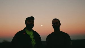 John Thayer and Ben Seretan stand silhouetted against a dusky gradient sky with a full moon between them. Photo by Lea Thomas.