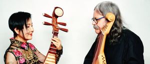 Min Xiao-Fen holds a pipa toward Julian Kytasty, who faces her with a bandura pressed to his cheek, against a white background. Photo by Pavlo Terekhov. Photo by Pavlo Terekhov.