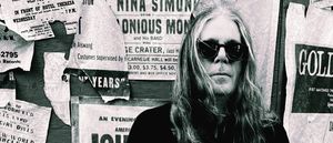 Bob Bert in dark sunglasses before a wall of torn vintage concert posters featuring Nina Simone and Thelonious Monk. Black-and-white. Credit: Michael Jung.