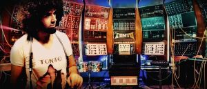 Robert Margouleff stands beside TONTO, a towering wall of modular synthesizer equipment, its patch cables spilling outward in every direction.