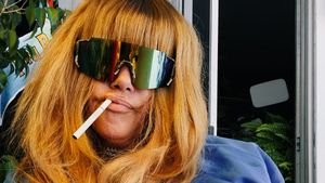 Close-up of Jennifer Herrema in mirrored shield sunglasses, a cigarette in her mouth and long strawberry-blond bangs framing her face.