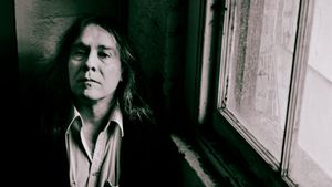 Martin Bisi leans against a wall beside a grimy window, looking into the camera, in a dark jacket over an open-collared shirt. Black and white.