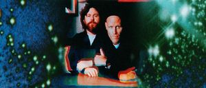 Gareth Quinn Redmond and Francis Harris sit together at a table in a grainy, color-shifted film still, framed by speckled blue and green light.