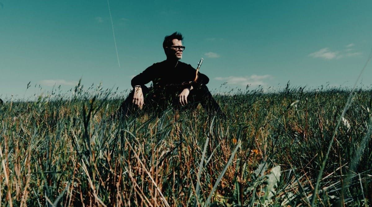 Donny McCaslin sitting in a field, saxophone nearby. Photo by Dave Stapleton.