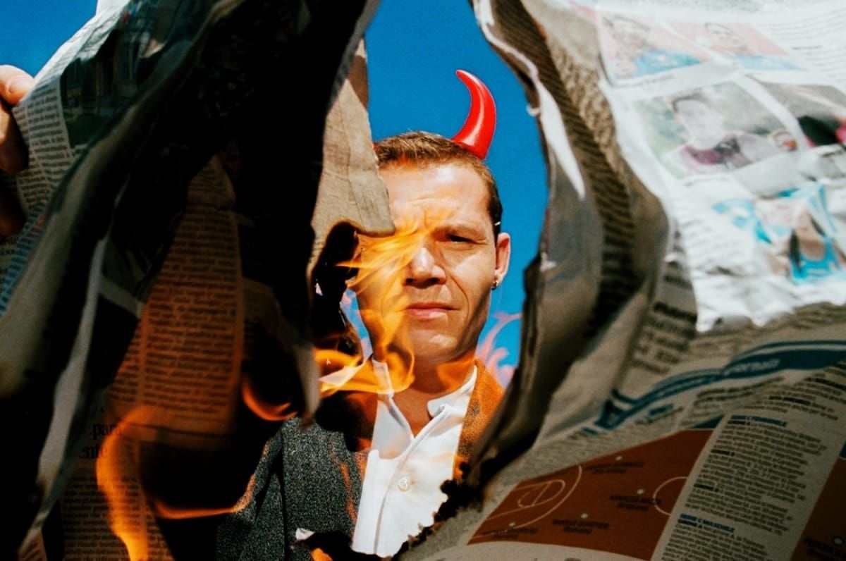 Westerman wearing devil horns and light a newspaper on fire. Photo by Eric Scaggiante.