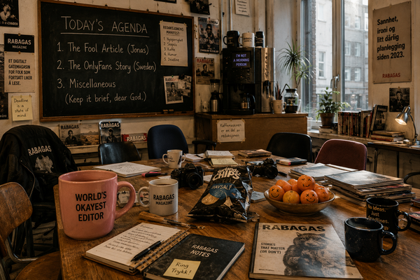A slightly cluttered editorial meeting room with a chalkboard agenda, coffee mugs, notebooks and an oversized pink mug, illuminated by soft Monday morning light.