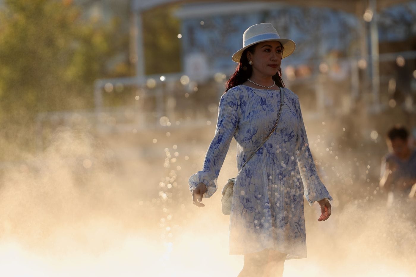 A woman in a white hat walking through golden backlit mist