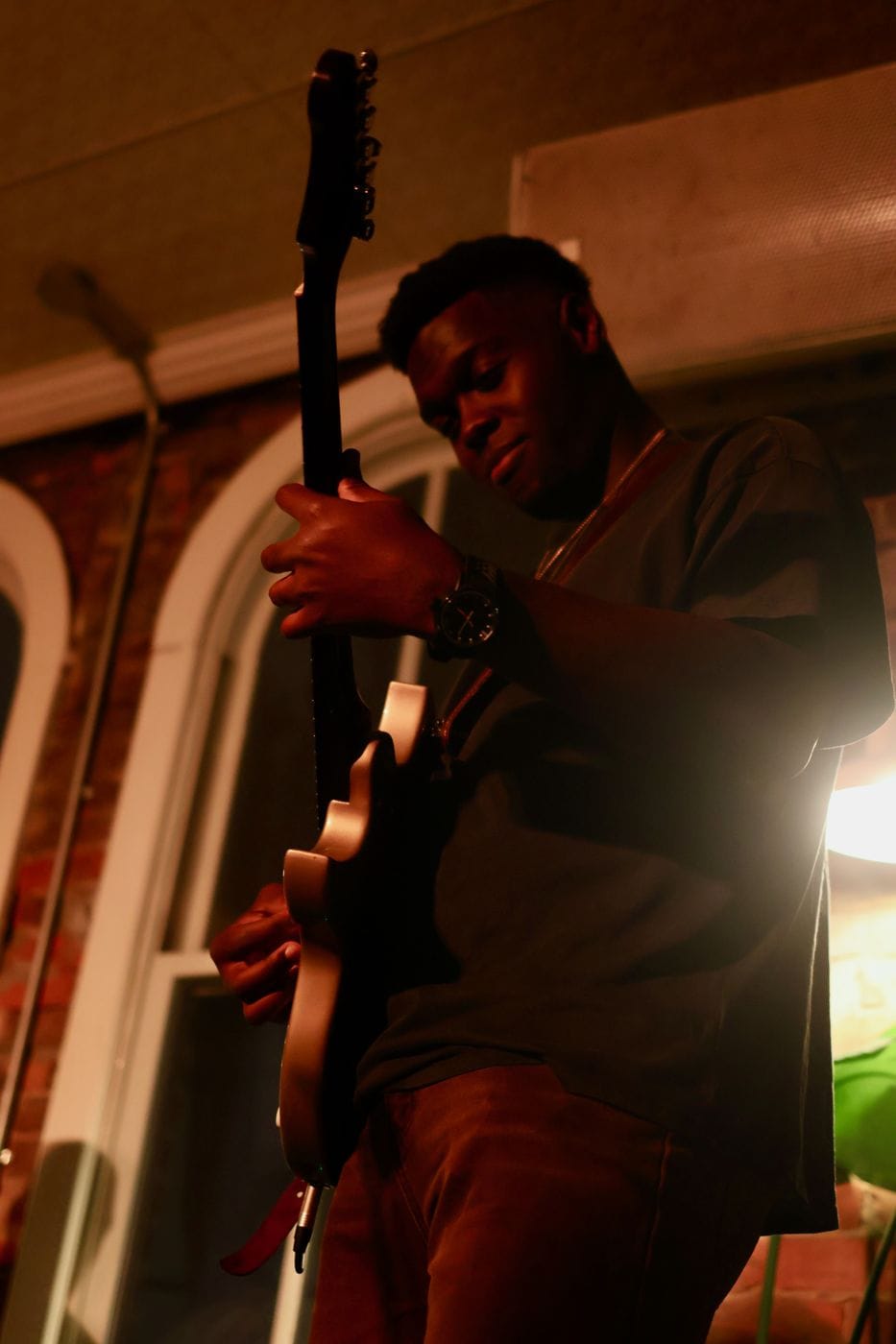 A guitarist bent over the neck of his instrument under a single warm lamp