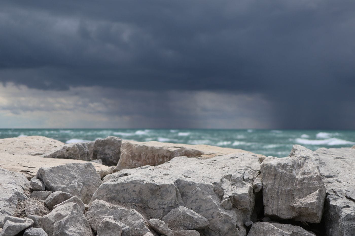 An August storm column over a lake breakwater, rain visible over the water