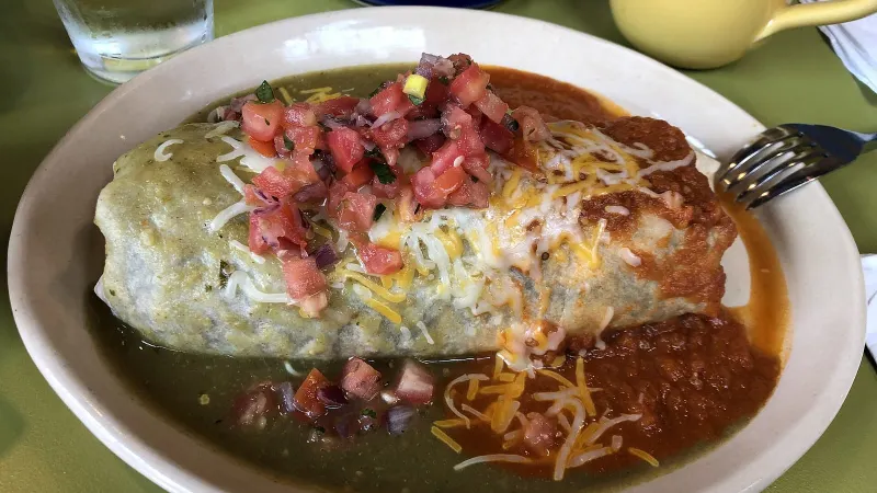 Breakfast burrito cut open on a plate with eggs and tortilla.
