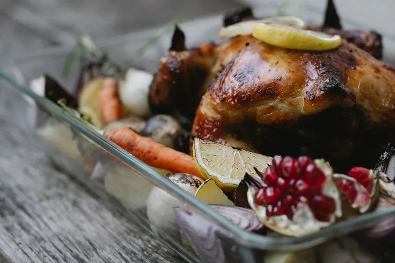 Roasted chicken with carrots, potatoes, and onions in a baking dish.