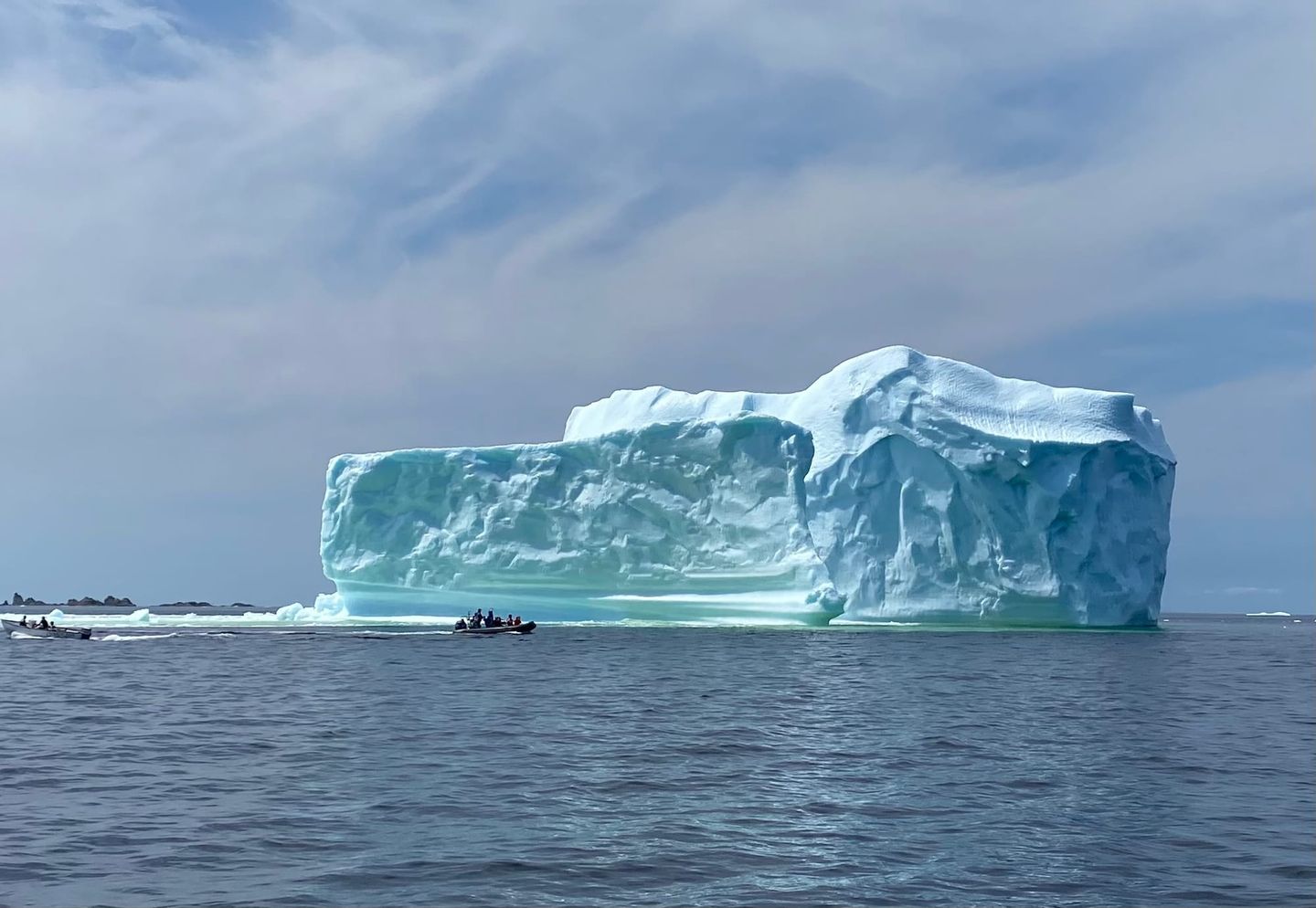 Large iceberg with a small boat of people beside it in Newfoundland