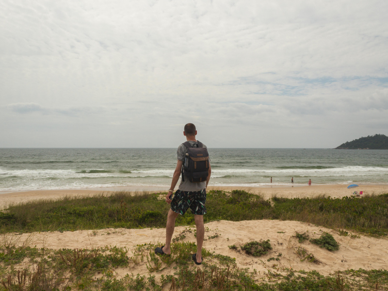 A male solo traveler with a backpack staring out over the ocean