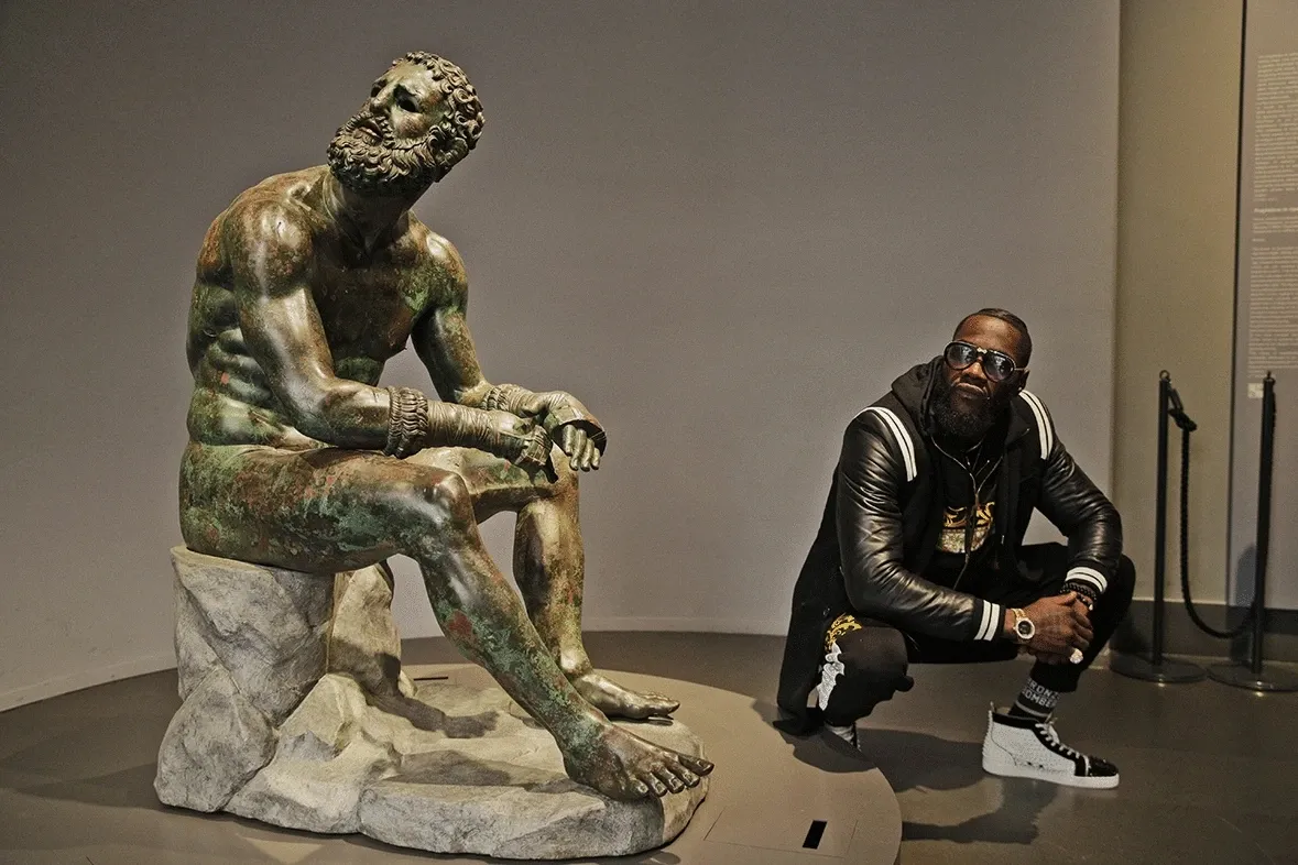 Deontay Wilder squatting next to the statue, 19 December 2019