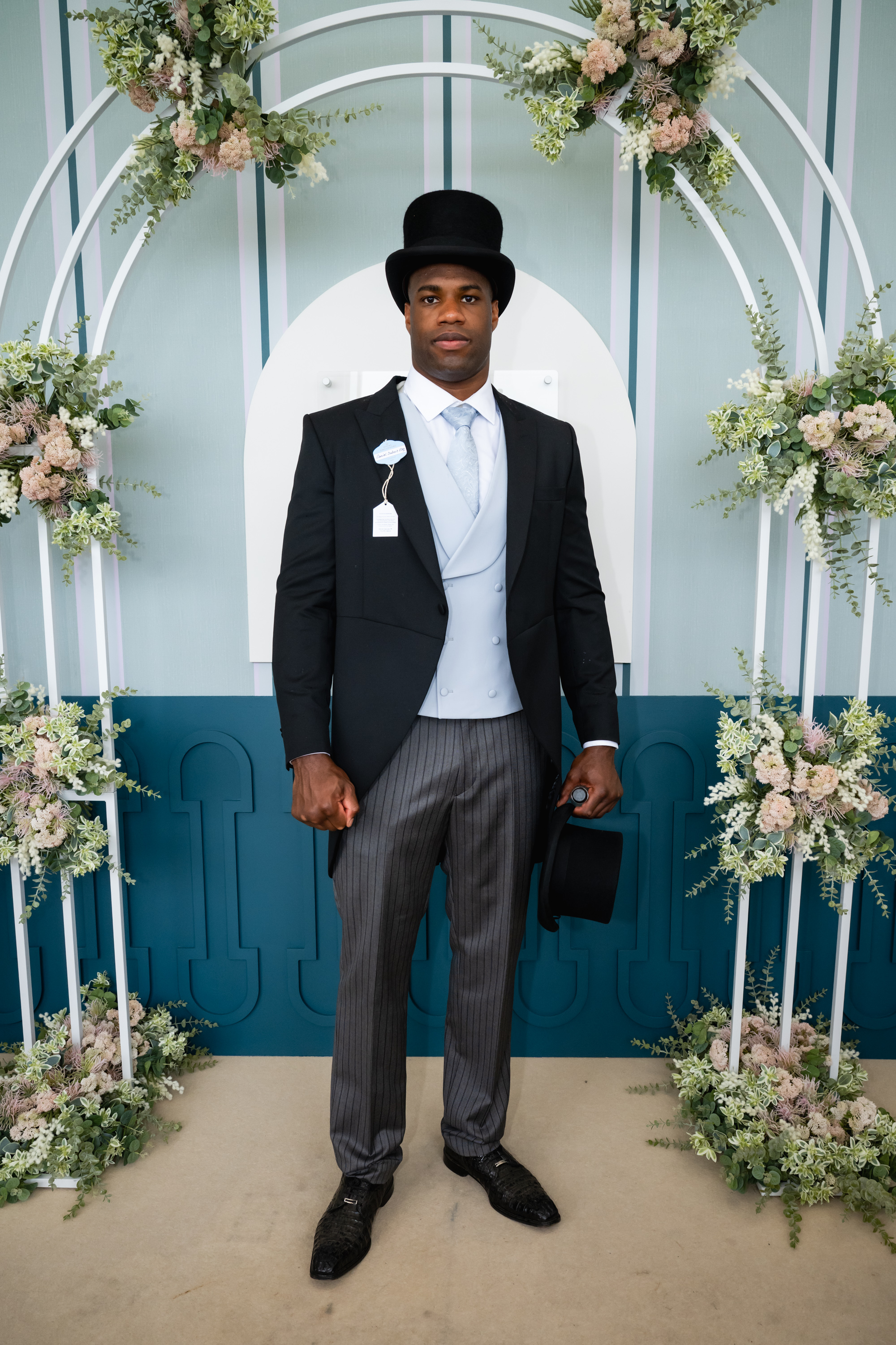 Daniel Dubois after nearly missing the Epsom Derby because he went to the wrong racetrack, he's posing for a photo dressed to the elevenses and is wearing a hat on his head in addition to holding one in his left hand for some unknown reason.