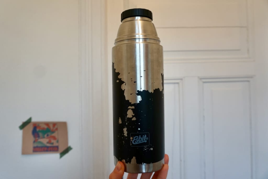 A hand holding a big thermos bottle by Esbit with heavy signs of usage