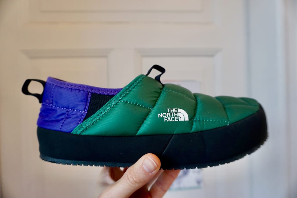 A hand holding a camp mule by The North Face, colored purple and green