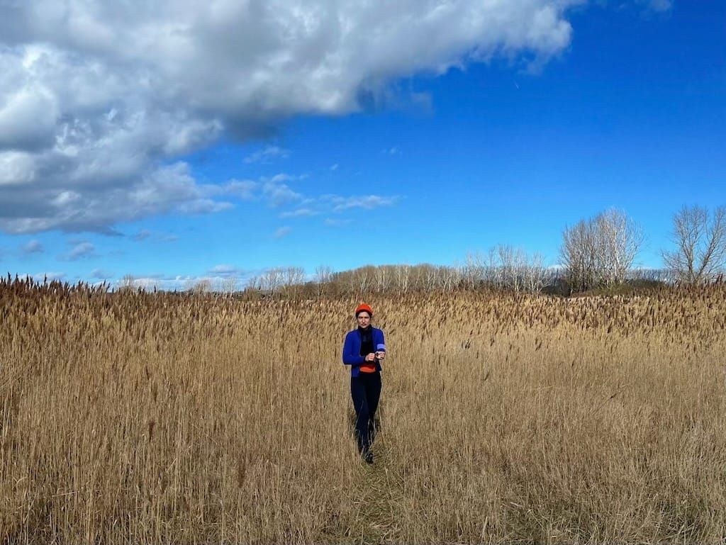 Stephanie wearing winter lycra and a tiny red beanie in a wintery field along the coast of the Baltic Sea
