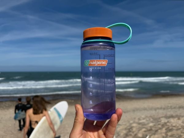 Purple 0.5L Nalgene water bottle in the forgeground, beach, waves and surfers in the background