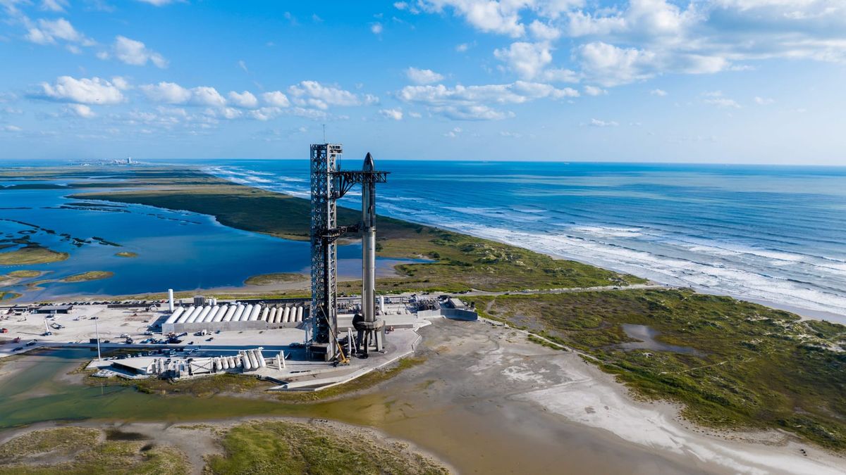 SpaceX Starship standing on its coastal launch pad beneath a bright blue sky.
