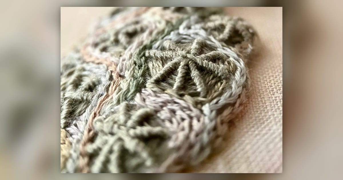 Close-up of raised grey and pale green embroidery testing layered stitches and rocky reef textures.