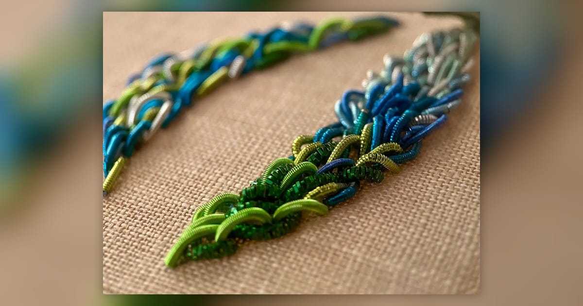Blue and green coiled wire embroidery samples arranged as dimensional seaweed on beige fabric.