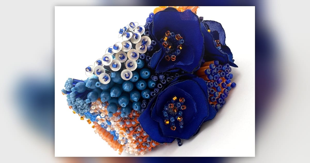 Sculptural blue embroidery bracelet combining fabric flowers, beads, sequins and orange accents.