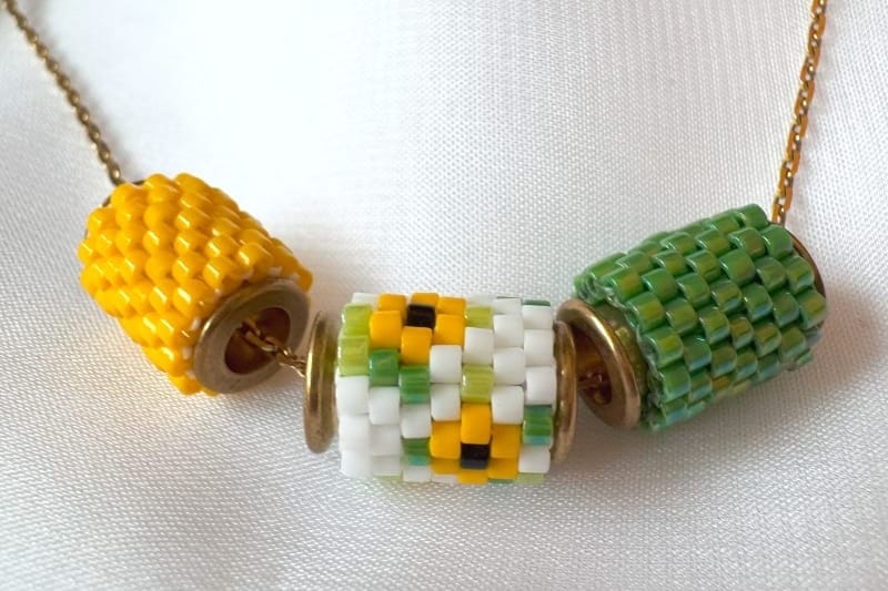 Three tubular peyote pendant elements in yellow, sunflower white, and green on a gold chain.
