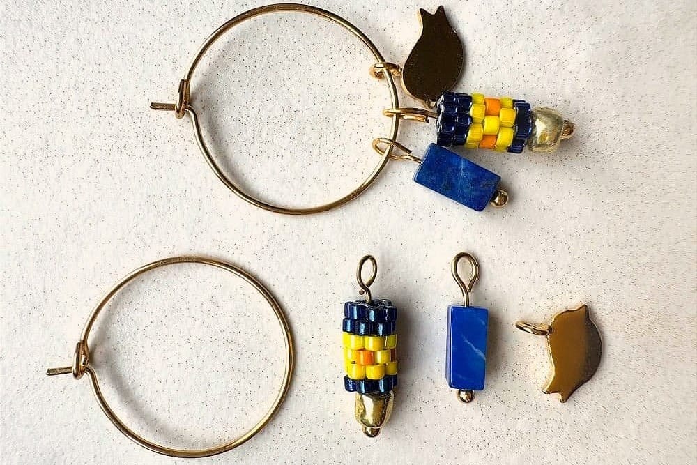 Gold-colored hoop earrings with blue and yellow beaded charms, blue stones, and gold-colored leaf charms.
