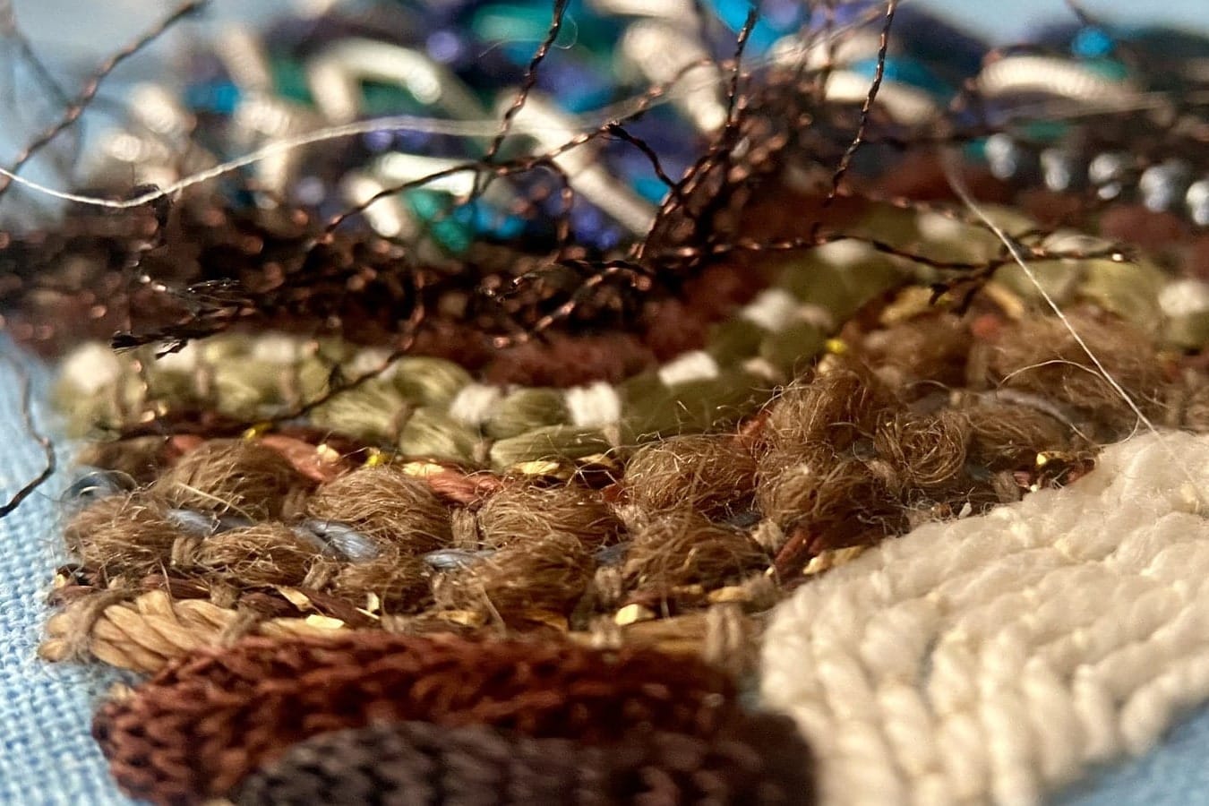 Brown, cream, and metallic embroidery textures with beads on pale blue fabric.