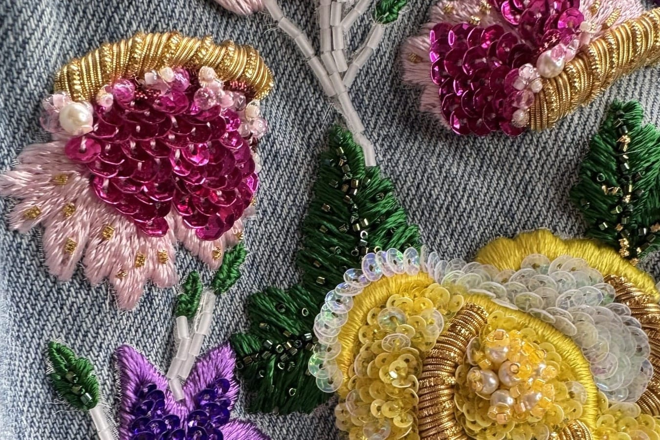 Pink, purple, and yellow flowers embroidered with sequins, beads, and gold-colored details on denim.