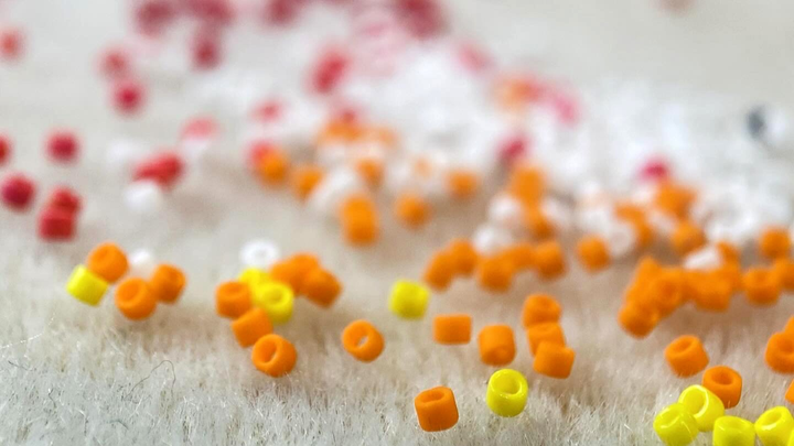 Orange, yellow, white, and red cylinder beads scattered across a pale work surface, photographed at close range with a shallow depth of field.