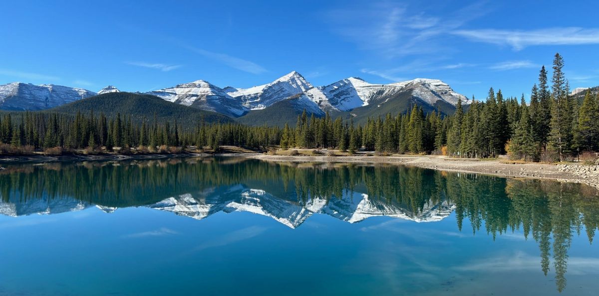 Snow-capped peaks and evergreens reflected in a calm mountain lake in Kananaskis Country