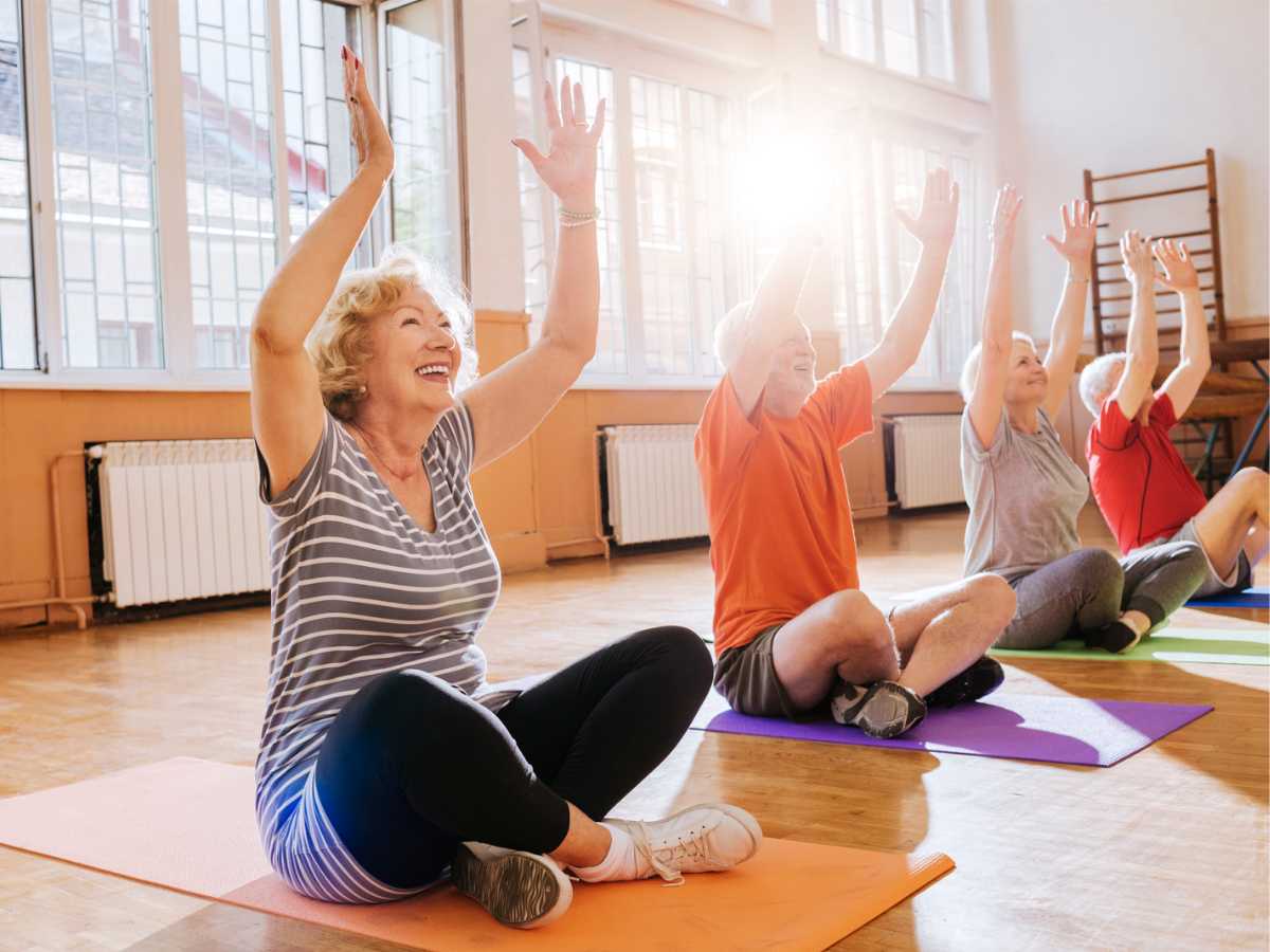 Cheerful seniors sitting on yoga mats and enjoying exercise together.