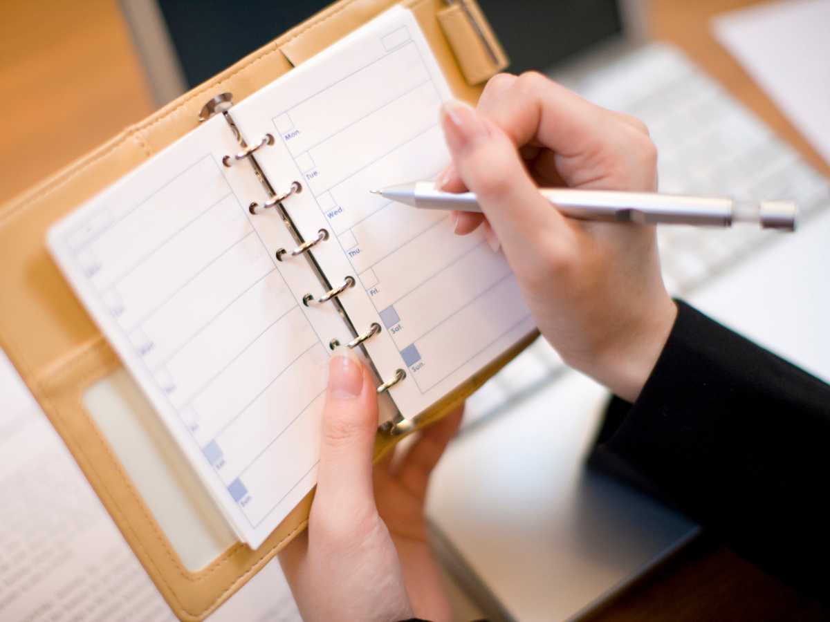 Woman writing her plans for day of the week on a planner.