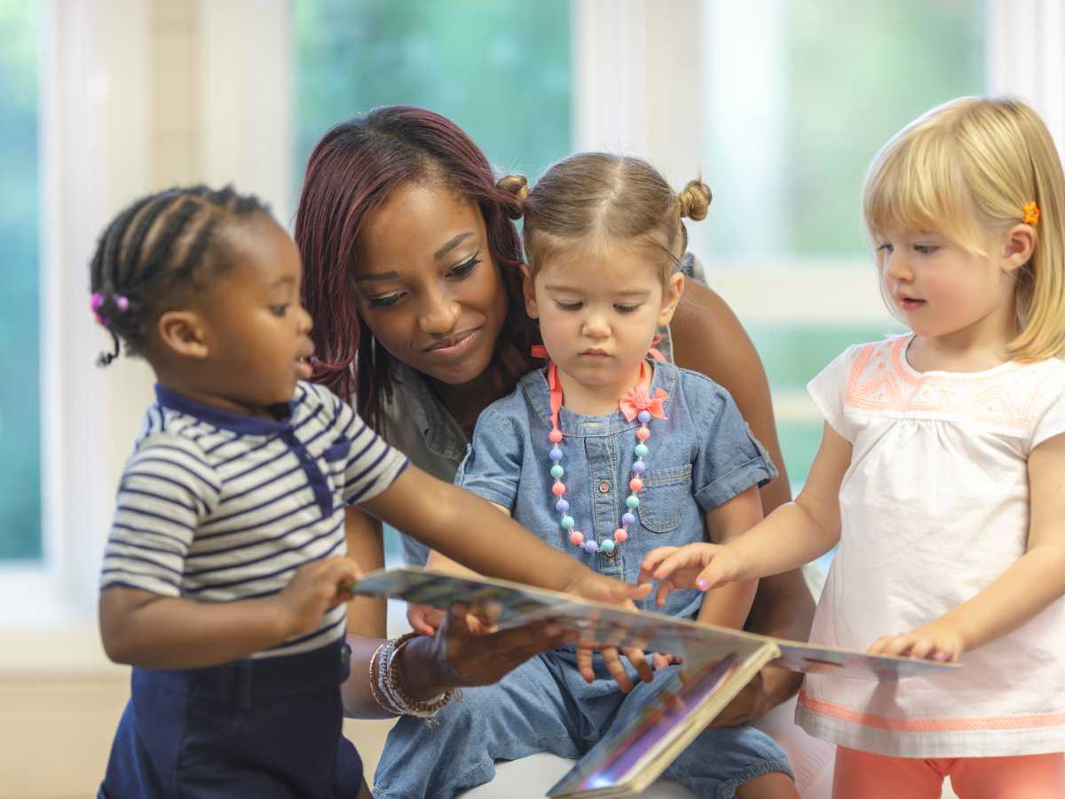Children of different backgrounds coming together to read a book with a teacher guiding them.