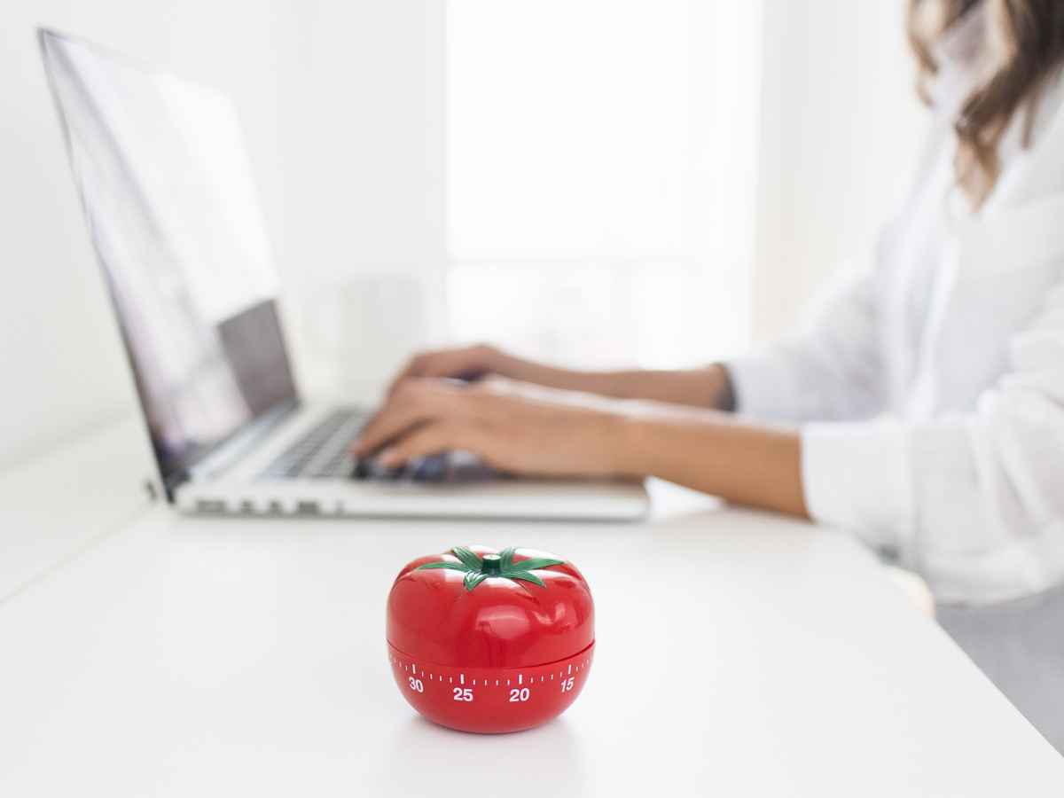 A woman working on her computer with a pomodoro timer to keep track of time on the side.