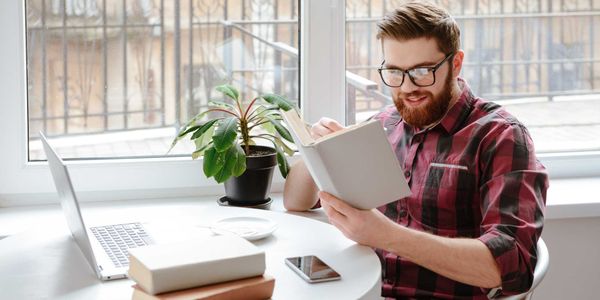 Studious man reading a book diligently at home in broad daylight.