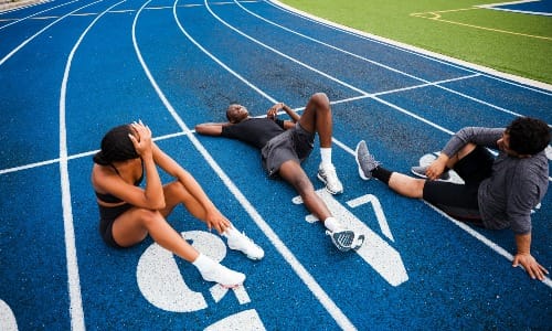 Athletes resting on a blue running track.
